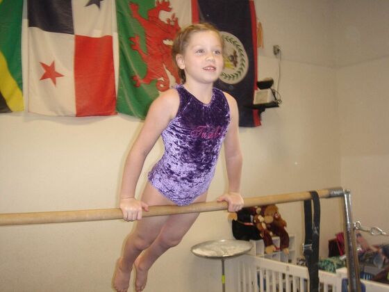 A young gymnast smiling as she swings on the bar