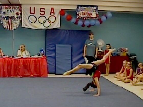 A gymnast mid-walkover on the floor while judges watch at Champion Day
